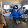 Chance joined the competition — help win amazing prizes! toddler, blue_jacket, sunglasses, beanie, indoor, kitchen_counter, wooden_ceiling, living_room, furniture, window, decor, rug, dog_tail, shoes, jeans, child, person, casual, cute, smiling