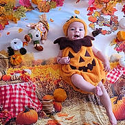 Filip participe au concours pour gagner de l'argent avec cette photo : baby, pumpkin_costume, fall_leaves, hay_bale, scarecrow, autumn, orange, white_pumpkin, black_pinecone, checkered_cloth, smiling, cute, child, holiday, festive, seasonal, background, playful, outfit, portrait