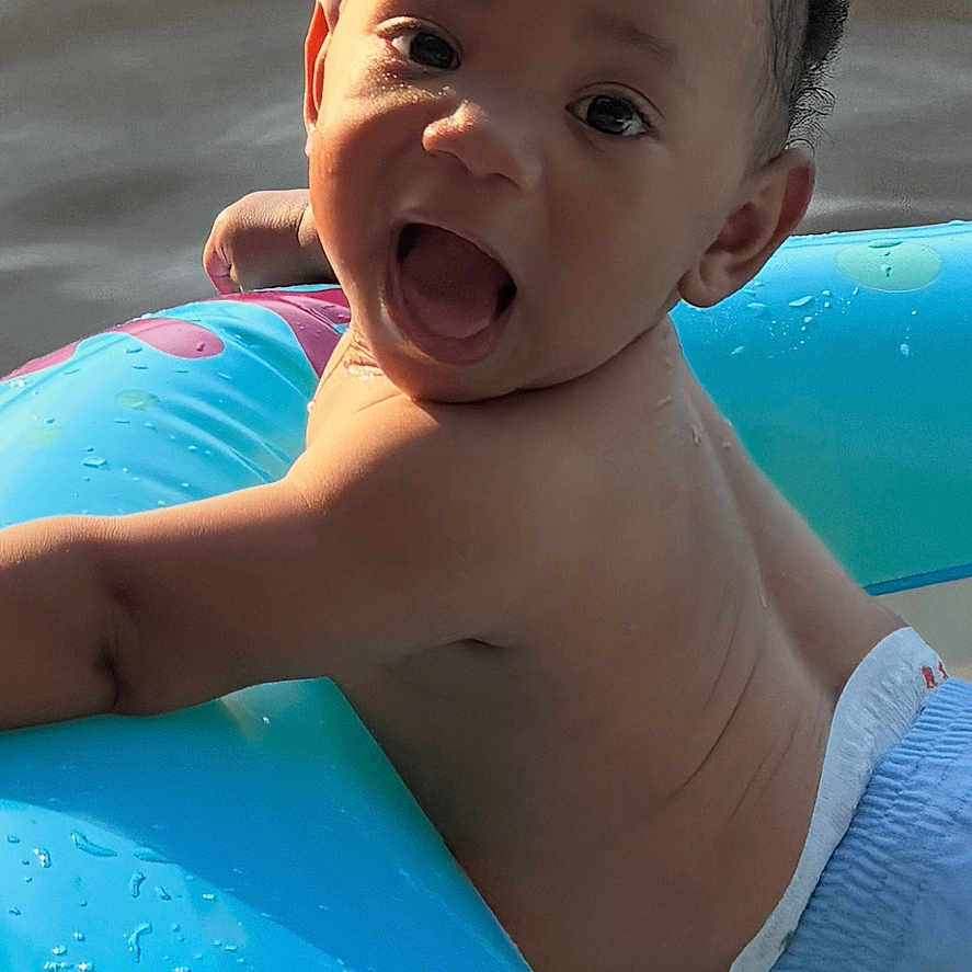 Zamir joined the competition — help win amazing prizes! baby, child, water, inflatable_ring, smiling, happy, sunlight, outdoor, play, summer, toddler, skin, diaper, closeup, face, person, water_droplets, floating, fun, joy