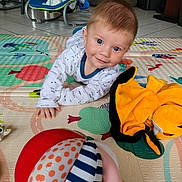 Charlie a rejoint le concours — aidez-le/la à gagner de superbes lots ! baby, child, playmat, toy, plush_toy, ball, crawling, floor, onesie, indoor, blue_eyes, smiling, hair, baby_rocker, colorful, patterned, tiled_floor, hand, face, person