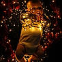 baby, infant, fairy_lights, christmas_lights, tinsel, onesie, glowing, festive, holiday, dark_background, cute, chubby, lying_down, decorations, red_tinsel, soft_lighting, small_child, portrait, holiday_theme, warm_light