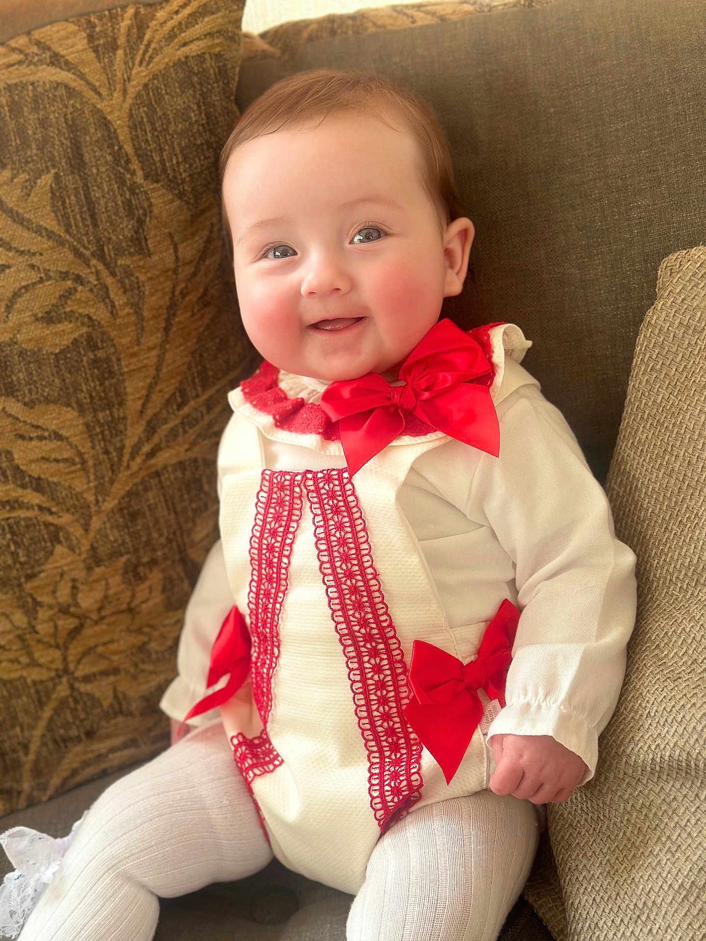 Lanesra joined the competition — help win amazing prizes! baby, child, smiling, couch, cushion, red_bow, white_outfit, lace, indoors, cute, portrait, happy, seated, infant, clothing, face, person, furniture, soft_lighting, cozy