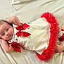 Lanesra is registered to the contest to win money with this photo: baby, infant, dress, red_bow, red_trim, white_sheet, lying_down, cute, child, footwear, socks, portrait, adorable, fashion, baby_clothes, closeup, person, indoor, young_child, resting