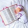 Gracie joined the competition — help win amazing prizes! baby, sleeping, infant, white_blanket, floral_hat, floral_clothing, open_book, text, soft_texture, peaceful, resting, cute, newborn, portrait, comfort, indoors, cozy, white_background, child, reading