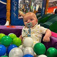 Lowen is registered to the contest to win money with this photo: baby, ball_pit, child, childcare, clothing, colorful_balls, curious, fun, indoor_playground, infant, leisure, netting, pacifier, padded_walls, plastic_balls, play_area, playtime, seated, soft_play, yellow_sun_pattern