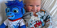 Lowen is registered to the contest to win money with this photo: baby, bed, blue, car_pattern, child, colorful, cuddly, cute, fabric, face, hair, happy, indoor, onesie, pillow, playful, plush_toy, seated, smile, soft_toy