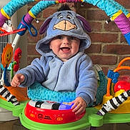 Ezra is registered to the contest to win money with this photo: baby, child, blue_onesie, eeyore_costume, baby_jumper, toy, colorful, brick_wall, happy, smiling, indoor, feet, playtime, cute, infant, hooded_clothing, person, early_childhood, home, entertainment