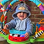 baby, child, blue_onesie, eeyore_costume, baby_jumper, toy, colorful, brick_wall, happy, smiling, indoor, feet, playtime, cute, infant, hooded_clothing, person, early_childhood, home, entertainment