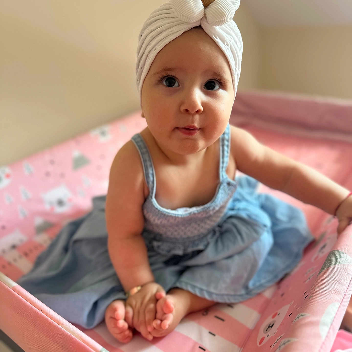 Evar is registered to the contest to win money with this photo: baby, blue, child, clothing, curious, cute, dress, flower, headwear, indoors, infant, person, pink, playpen, portrait, sitting, skin, small_feet, turban, wide_eyes