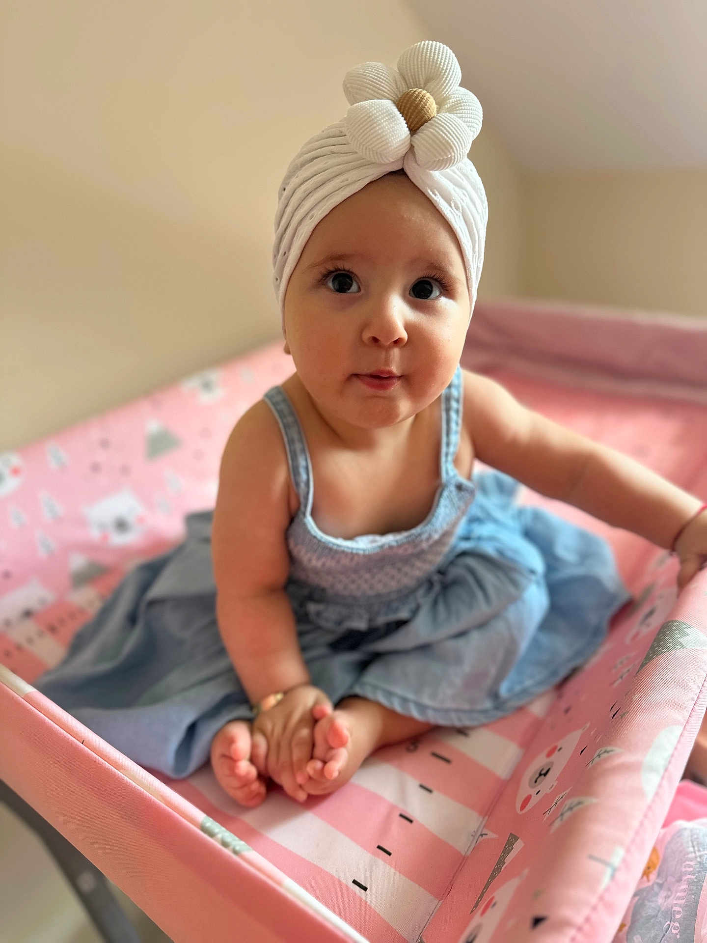 Evar is registered to the contest to win money with this photo: baby, blue, child, clothing, curious, cute, dress, flower, headwear, indoors, infant, person, pink, playpen, portrait, sitting, skin, small_feet, turban, wide_eyes