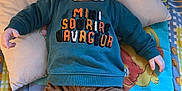 Matias participe au concours pour gagner de l'argent avec cette photo : baby, smiling, child, infant, sweatshirt, corduroy_pants, pillow, blanket, patterned_blanket, happy, lying_down, footwear, indoors, cute, portrait, clothing, playful_text, colorful, young_child, cozy