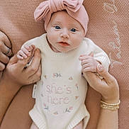 Tatum is registered to the contest to win money with this photo: baby, infant, pink_bow, white_sweater, hands, blanket, blue_eyes, cute, newborn, holding_hands, soft_texture, portrait, child, family, skin, nails, bracelets, buttoned_clothing, lying_down, close_up
