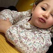 Anaïs a rejoint le concours — aidez-le/la à gagner de superbes lots ! child, toddler, face, winking, puckered_lips, floral_shirt, long_sleeves, table, wooden_table, indoor, curly_hair, light_skin, closeup, portrait, playful, expression, person, casual, young, cute
