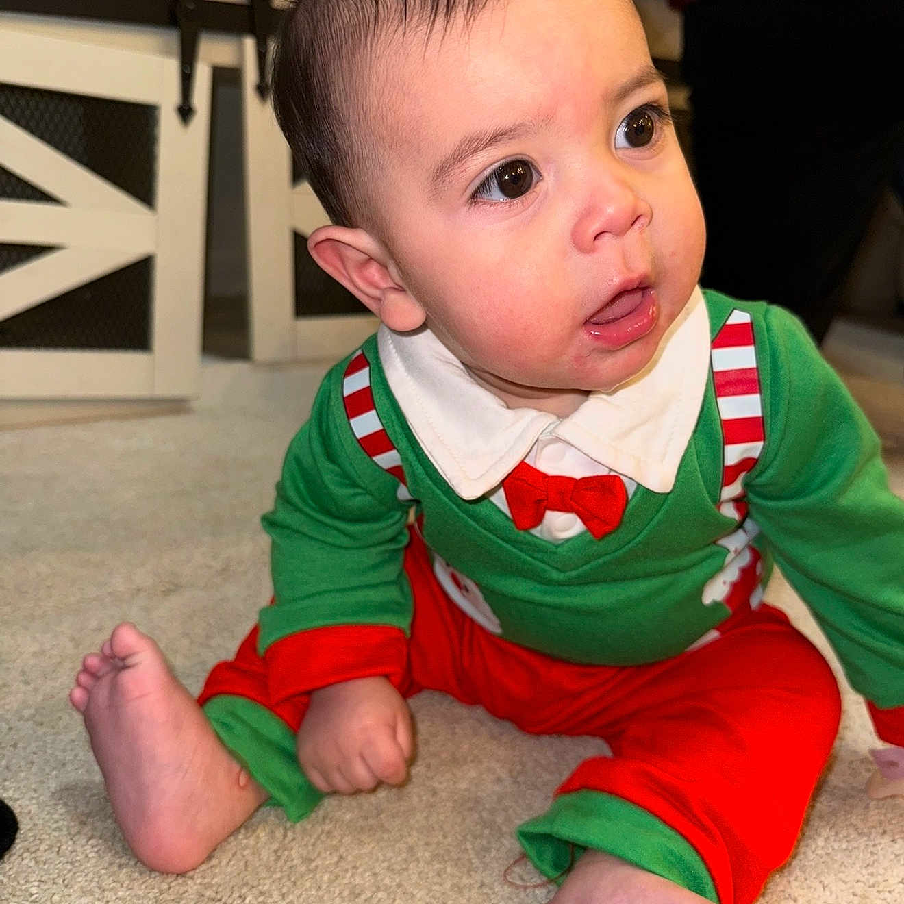 Thiago is registered to the contest to win money with this photo: baby, candid, carpet, child, curious, cute, expression, festive_outfit, floor, green_clothing, holiday_clothes, indoor, infant, open_mouth, person, red_clothing, sitting, toddler, wide_eyes, young_child