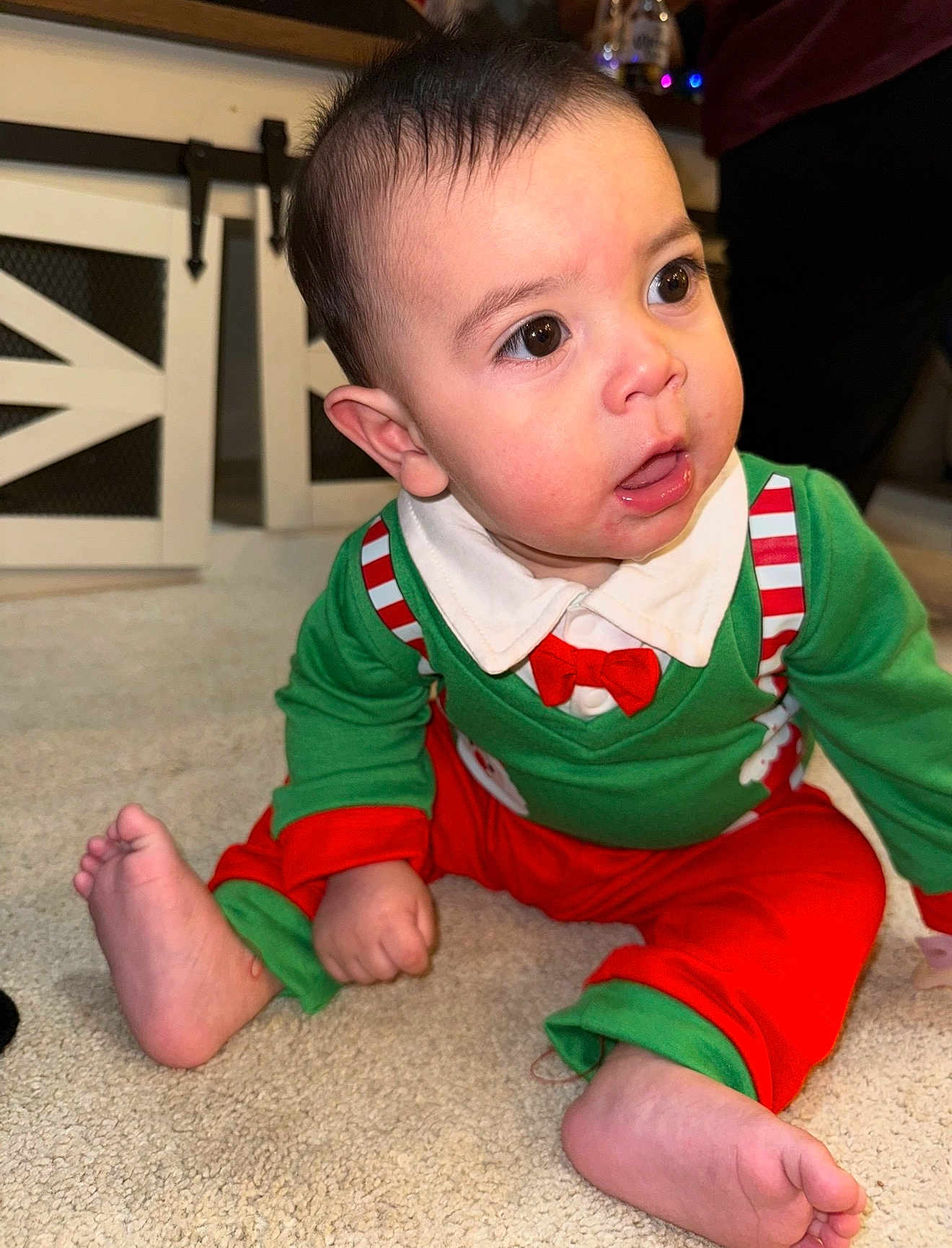 Thiago is registered to the contest to win money with this photo: baby, child, infant, sitting, carpet, green_clothing, red_clothing, festive_outfit, indoor, cute, curious, wide_eyes, open_mouth, person, toddler, candid, young_child, floor, holiday_clothes, expression