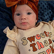 Zyah is registered to the contest to win money with this photo: baby, infant, child, face, headband, bow, clothing, shirt, text, blanket, couch, indoor, portrait, cute, expression, skin, person, cozy, soft, comfortable