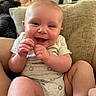 baby, smiling, happy, infant, cushion, indoor, person, face, skin, clothing, legs, hand, cute, child, young, sitting, comfort, home, joy, expression