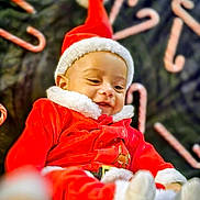 Tommy is registered to the contest to win money with this photo: baby, child, santa_hat, christmas_outfit, red_clothing, white_fur_trim, candy_cane, holiday, festive, smiling, cute, cozy, background, lying_down, celebration, seasonal, happy, infant, portrait, soft