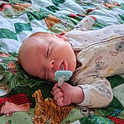 Braxton is registered to the contest to win money with this photo: baby, newborn, infant, sleeping, pacifier, blanket, quilt, bed, portrait, face, hand, fingers, clothing, onesie, cartoon, animals, patterned_fabric, indoors, cozy, closeup
