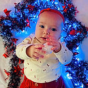 Lucie participe au concours pour gagner de l'argent avec cette photo : baby, infant, child, red_clothing, white_shirt, headband, holiday_lights, decorations, blue_lights, red_stars, festive, cute, portrait, indoors, hands, face, expression, background, celebration, warm