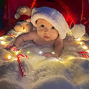 Lucie a rejoint le concours — aidez-le/la à gagner de superbes lots ! baby, blanket, candy_cane, child, christmas, cute, decorations, fairy_lights, festive, holiday, indoors, infant, plush, portrait, red, santa_hat, smiling, soft_texture, teddy_bear, white