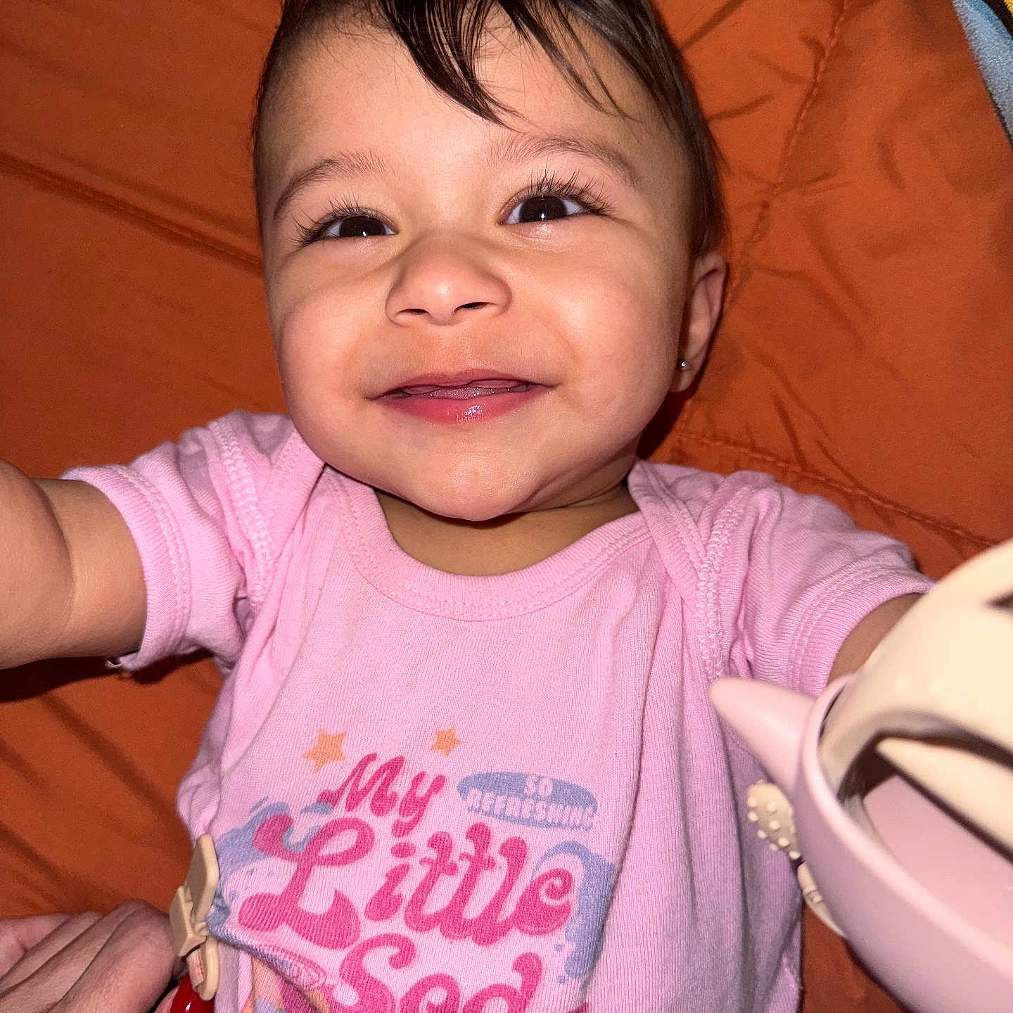 Arianna joined the competition — help win amazing prizes! baby, smiling, child, pink_shirt, text, toy, hand, orange_blanket, face, cute, infant, portrait, happy, sleeves, lying_down, closeup, person, eyelashes, skin, clothing