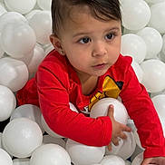 Arianna joined the competition — help win amazing prizes! toddler, child, red_shirt, ball_pit, white_balls, indoor, cute, curious, young_child, play, fun, portrait, face, hand, person, short_hair, earring, bright_color, expression, sitting