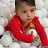 toddler, child, red_shirt, ball_pit, white_balls, indoor, cute, curious, young_child, play, fun, portrait, face, hand, person, short_hair, earring, bright_color, expression, sitting