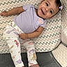 Arianna is registered to the contest to win money with this photo: baby, child, smiling, purple_clothing, pants, bow, earrings, patterned_cushion, zigzag_pattern, sea_creature_print, octopus, seahorse, starfish, whale, crab, indoor, soft_lighting, happy, lying_down, cute