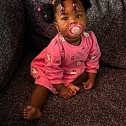Kennayah a rejoint le concours — aidez-le/la à gagner de superbes lots ! baby, child, girl, pacifier, pink_dress, hair_beads, sitting, couch, indoors, cute, portrait, smiling, infant, young_child, clothing, foot, hand, skin, furniture, comfort