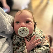 Summer is registered to the contest to win money with this photo: baby, pacifier, infant, floral_clothing, closeup, person, hand, face, newborn, soft_focus, indoor, portrait, cute, child, holding, young, warm, cozy, comfort, sitting