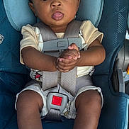 Kian is registered to the contest to win money with this photo: baby, child, car_seat, safety_harness, socks, clothing, face, hands, legs, seat, warning_label, infant, cute, wide_eyes, tongue_out, person, indoor, seatbelt, baby_clothes, closeup