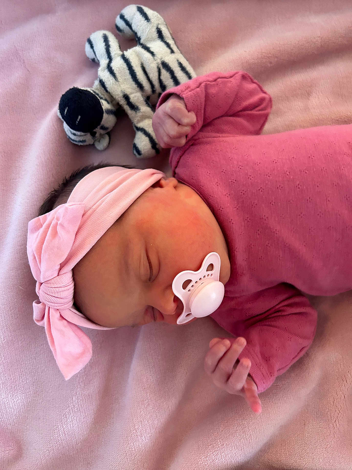 Amari joined the competition — help win amazing prizes! baby, newborn, pacifier, headband, pink_clothing, pink_blanket, sleeping, plush_toy, zebra_pattern, infant, cute, soft_texture, peaceful, child, resting, indoors, portrait, small_hands, cozy, adorable
