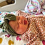 baby, sleeping, headband, floral_clothing, blanket, duck_pattern, striped_cloth, infant, cute, peaceful, soft_texture, bed, newborn, child, face, mouth_open, indoor, portrait, resting, cozy