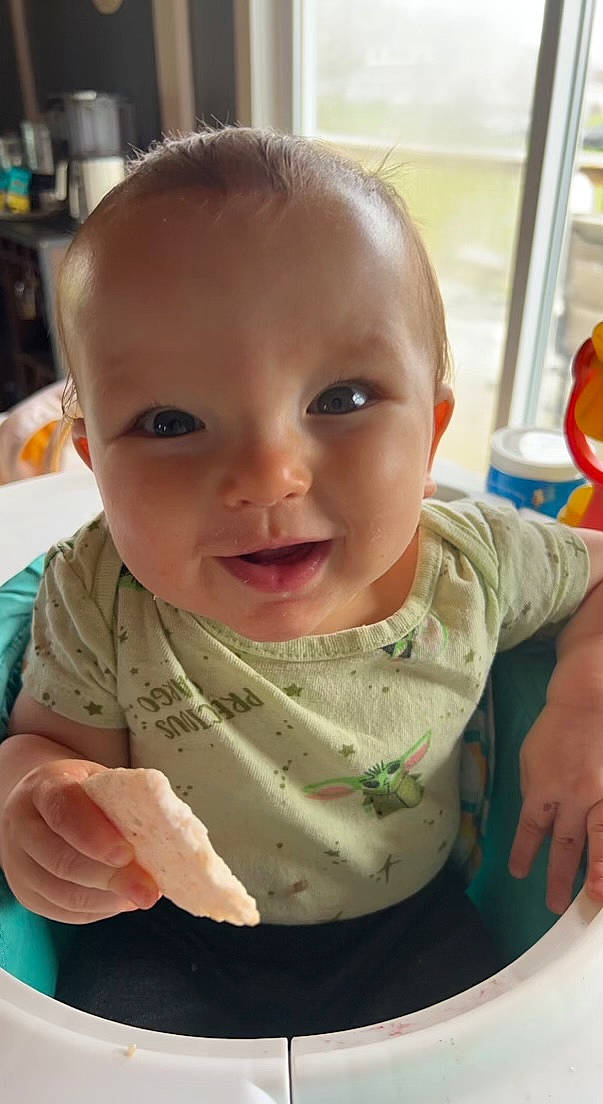 Theo is registered to the contest to win money with this photo: arm, baby, baby_playing_with_food, baby_toddler_clothing, cheek, child, chin, eyebrow, face, facial_expression, finger, iris, lip, mouth, nose, people, person, skin, sleeve, smile