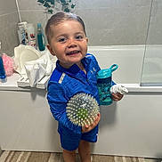 Tommy-lee joined the competition — help win amazing prizes! toddler, child, bathroom, blue_clothing, spiky_ball, sippy_cup, smiling, hair, floor_rug, plant, bathtub, bath_items, toy, footwear, person, indoor, happy, standing, young_child, casual