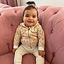 baby, child, smile, sitting, pink_couch, jacket, pants, shoes, hair_tie, indoors, cute, happy, plush_furniture, portrait, young_child, cozy, buttoned_jacket, tufted_couch, small_hands, casual_wear