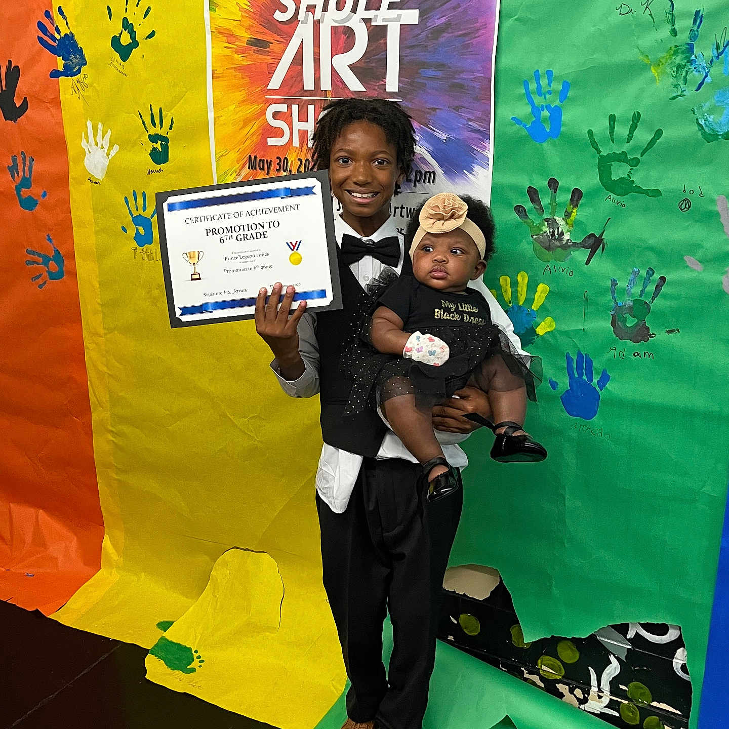 Princes Damiya joined the competition — help win amazing prizes! child, baby, tuxedo, certificate, promotion, art_show, handprints, colorful_backdrop, school_event, smiling, portrait, indoor, celebration, person, clothing, headband, shoes, floor, holding, happy