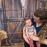Stevie joined the competition — help win amazing prizes! baby, woman, glasses, barn_door, rustic, cowboy_boot, hay_bale, smile, holding, indoor, casual_clothing, portrait, child, person, background, wood, hair, happy, toddler, family