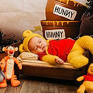Stevie is registered to the contest to win money with this photo: baby, sleeping, costume, winnie_the_pooh, yellow, red_shirt, bed, plush_toys, tigger, eeyore, pooh, piglet, honey_pots, wooden_floor, cute, child, indoor, toy, soft_toys, resting