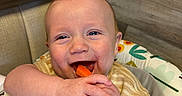 Kayson joined the competition — help win amazing prizes! baby, child, high_chair, carrot, food, smile, happy, cute, infant, hands, face, chewing, clothing, pattern, fabric, indoor, wood, seat, playful, colorful