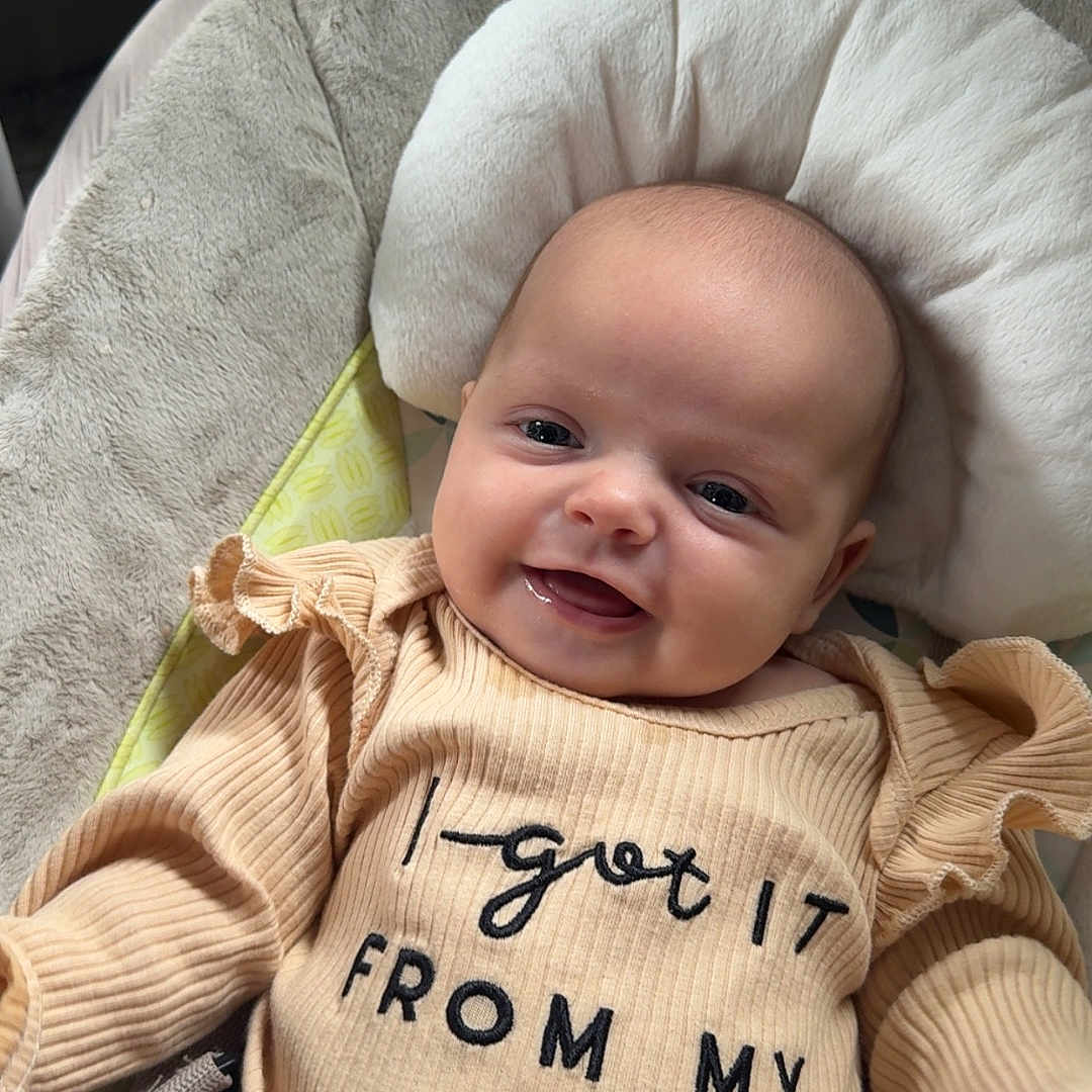 Kenidy joined the competition — help win amazing prizes! apparel, baby, beige, child, closeup, clothing, cushion, cute, face, happy, head, indoors, infant, person, portrait, seat, smiling, soft_texture, text_on_clothing, young_child