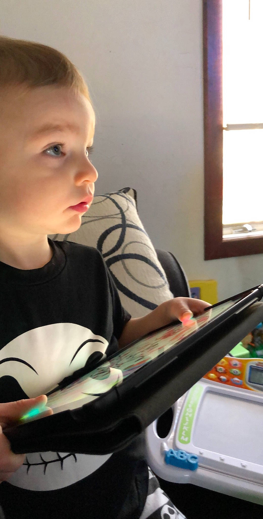Daxton is registered to the contest to win money with this photo: arm, automotive_design, book, child, electronic_device, fun, gadget, hand, lap, musician, office_equipment, person, publication, reading, sitting, snapshot, standing, t_shirt, toddler, window