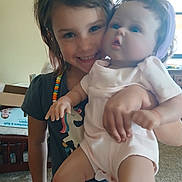 Laila is registered to the contest to win money with this photo: child, doll, indoor, smile, happy, girl, toy, clothing, face, person, carpet, furniture, necklace, short_hair, baby_doll, holding, play, cute, room, casual