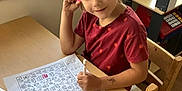 Laila joined the competition — help win amazing prizes! child, girl, braided_hair, red_shirt, marker, worksheet, table, chair, classroom, educational_toys, window, wooden_furniture, indoor, learning, playroom, pens, basket, thoughtful, seated, young
