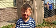 Meeko is registered to the contest to win money with this photo: child, toddler, boy, striped_shirt, smiling, outdoor, playhouse, toy, yellow_shovel, grass, fence, sunny, daytime, plastic, yard, happy, person, playing, casual_clothing, short_hair