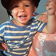 Meeko is registered to the contest to win money with this photo: child, boy, helmet, striped_shirt, smiling, indoor, pink_blanket, adidas_logo, happy, portrait, casual_clothing, face, person, young, seated, motion_blur, home, playful, cute, cheerful