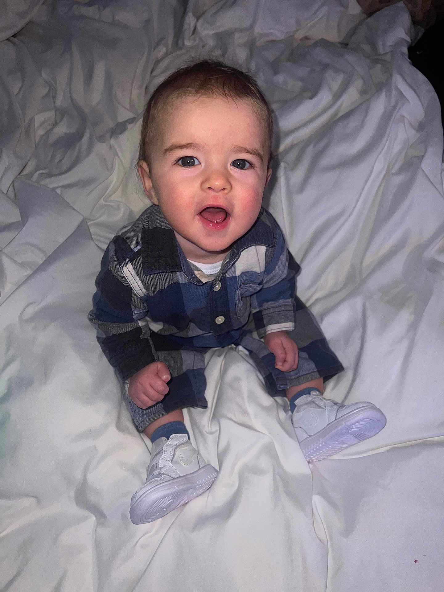 Rowan is registered to the contest to win money with this photo: baby, child, infant, plaid_shirt, white_sneakers, bed, blanket, indoor, person, smiling, happy, cute, young_child, clothing, feet, sitting, expression, face, skin, hair
