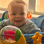 Kaleo is registered to the contest to win money with this photo: baby, infant, smiling, dimple, toy, activity_center, play_seat, plastic_toy, indoor, window, face, eyes, mouth, ears, hooded_clothing, happy, portrait, colorful, cheeks, child