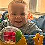 baby, infant, smiling, dimple, toy, activity_center, play_seat, plastic_toy, indoor, window, face, eyes, mouth, ears, hooded_clothing, happy, portrait, colorful, cheeks, child